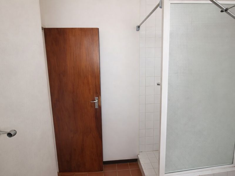 A functional bathroom featuring a tiled shower enclosure and a timber door, presenting a clean but dated aesthetic ready for modernization.