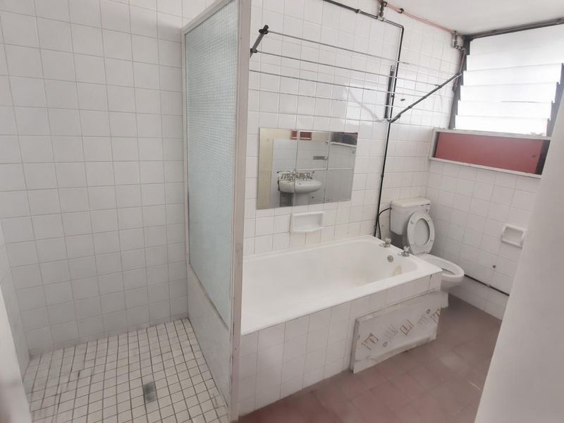 A dated bathroom featuring a combined bathtub and shower area, tiled walls, and a louvered window, offering potential for a modern renovation.