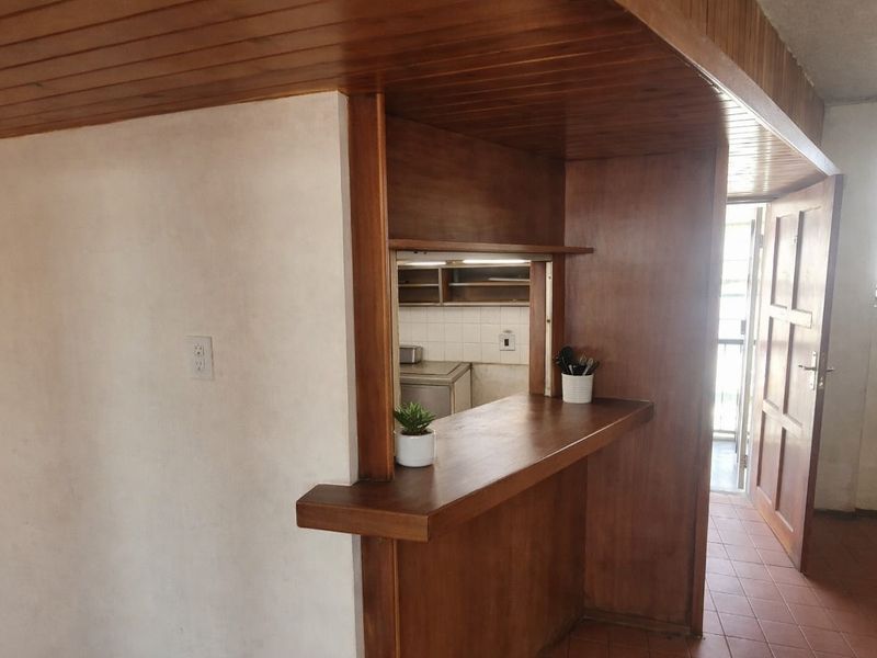 Open plan living area featuring a timber breakfast bar, wood-paneled ceiling, and a convenient pass-through window connecting to the kitchen space.