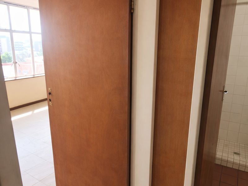 A view from a hallway looking into an adjacent room and a tiled bathroom area, featuring wooden doors and neutral floor tiles.
