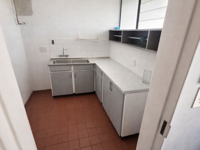 A compact, functional kitchen featuring a double stainless steel sink, laminate countertops, tiled backsplash, and ample built-in cabinetry with open shelving.