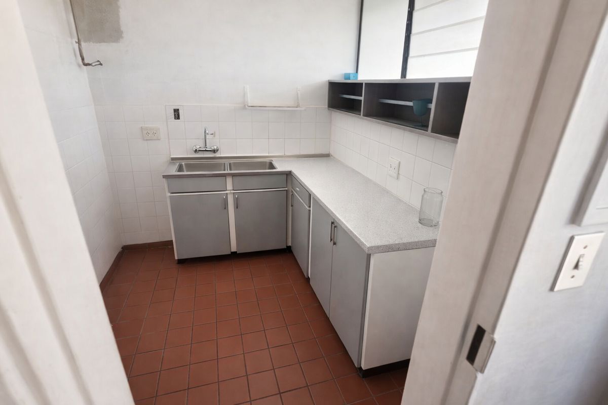 A compact, functional kitchen featuring a double stainless steel sink, laminate countertops, tiled backsplash, and ample built-in cabinetry with open shelving.