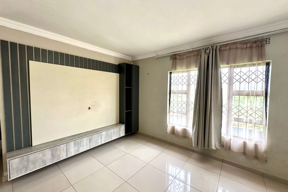 A bright living room featuring large format floor tiles, crown molding, and a modern built-in media unit with integrated shelving.