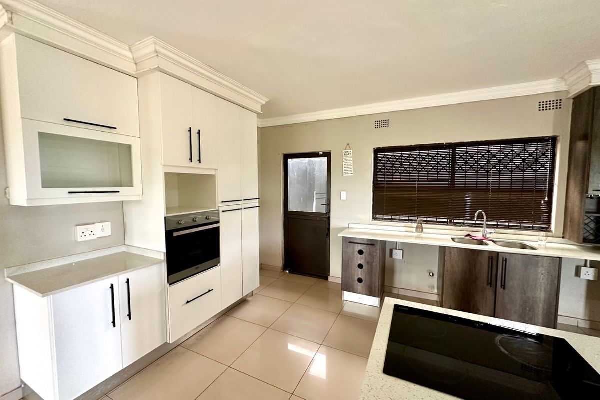A spacious kitchen featuring white and dark wood cabinetry, stone countertops, built-in oven, electric hob, and tiled flooring with direct exterior access.