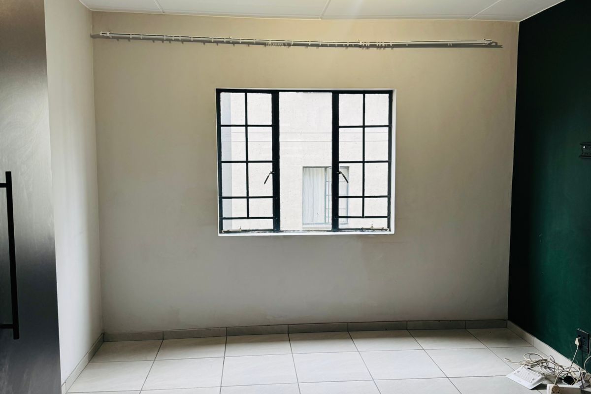 An empty bedroom featuring tiled flooring, a grid-pattern window, and a dark green accent wall, providing a blank canvas for personalization.