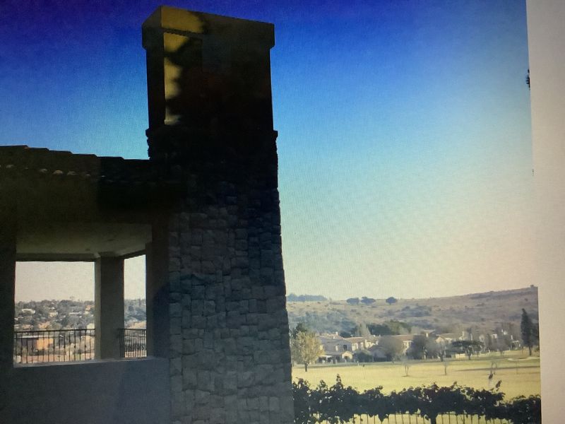 A covered patio area featuring a prominent stone-clad chimney and wrought iron railing, offering expansive views of the surrounding landscape.