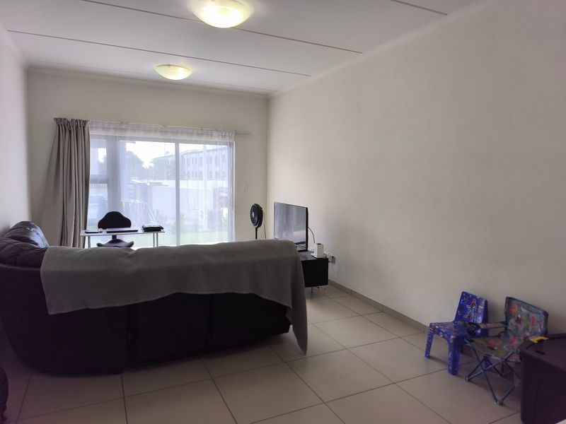A spacious living room featuring neutral tiled flooring and a large sliding glass door that provides natural light and access to the exterior.