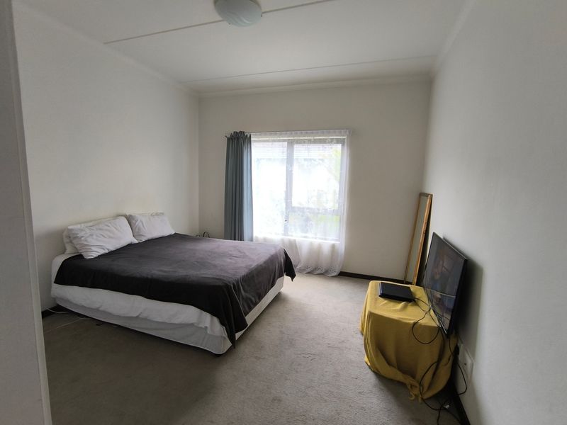 A standard bedroom featuring neutral walls, carpeted flooring, and a large window with curtain tracks, providing a functional and well-lit living space.