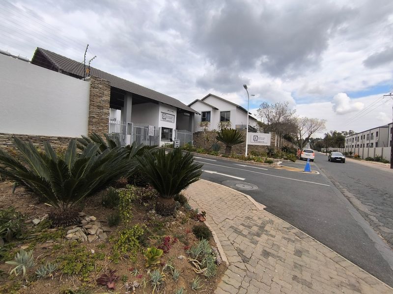 Front exterior view of the apartment complex entrance, featuring stone cladding, secure gated access, electric fencing, and well-maintained landscaped surroundings.