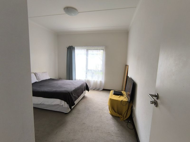 A standard bedroom featuring carpeted flooring, a central ceiling light, and a window providing natural light.