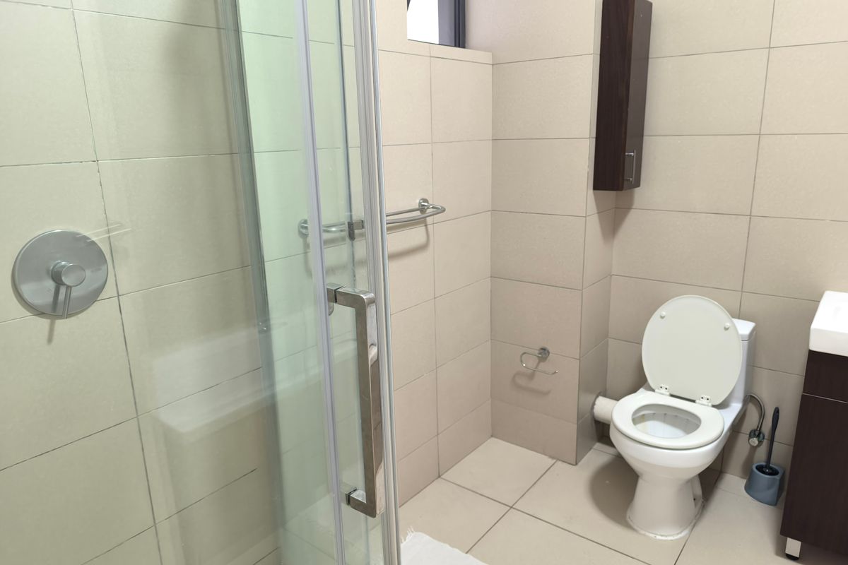 A clean, modern bathroom featuring a glass-enclosed shower, wall-mounted toilet, neutral tiled finishes, and a vanity unit with integrated storage.