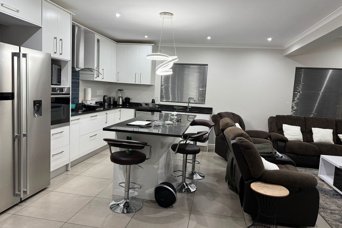 Modern open-plan kitchen and living area featuring a central island with granite countertops, sleek white cabinetry, and integrated appliances.