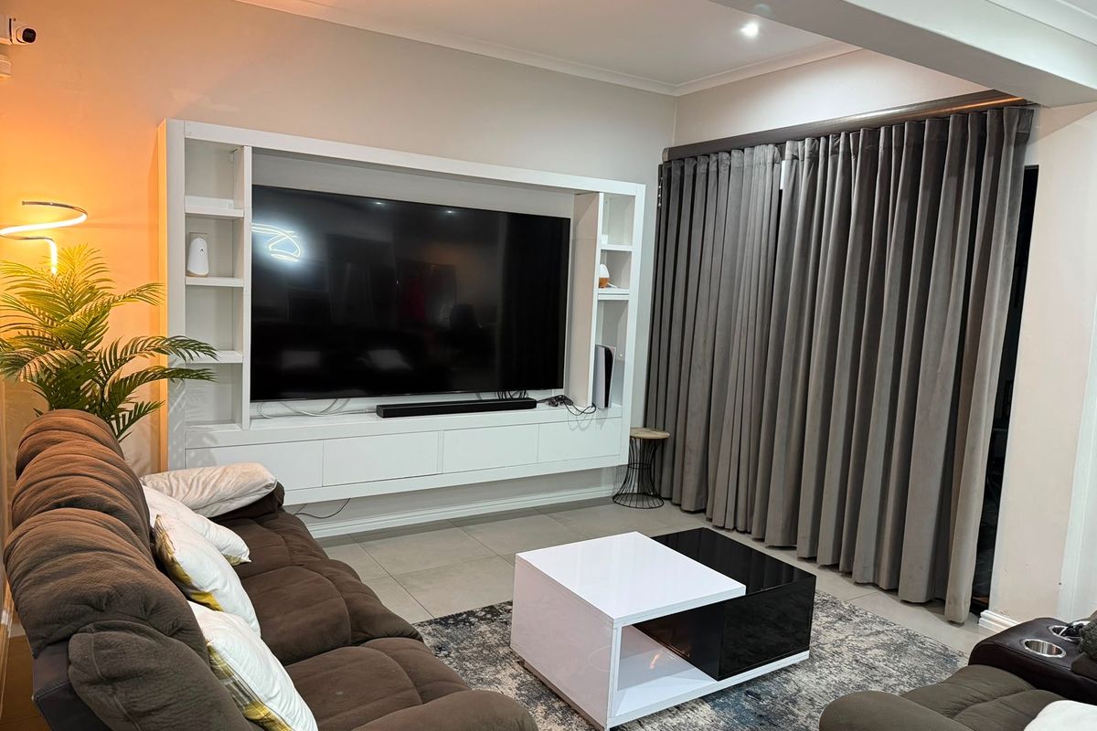 A well-maintained living room featuring a large built-in media unit, tiled flooring, and floor-to-ceiling curtains.