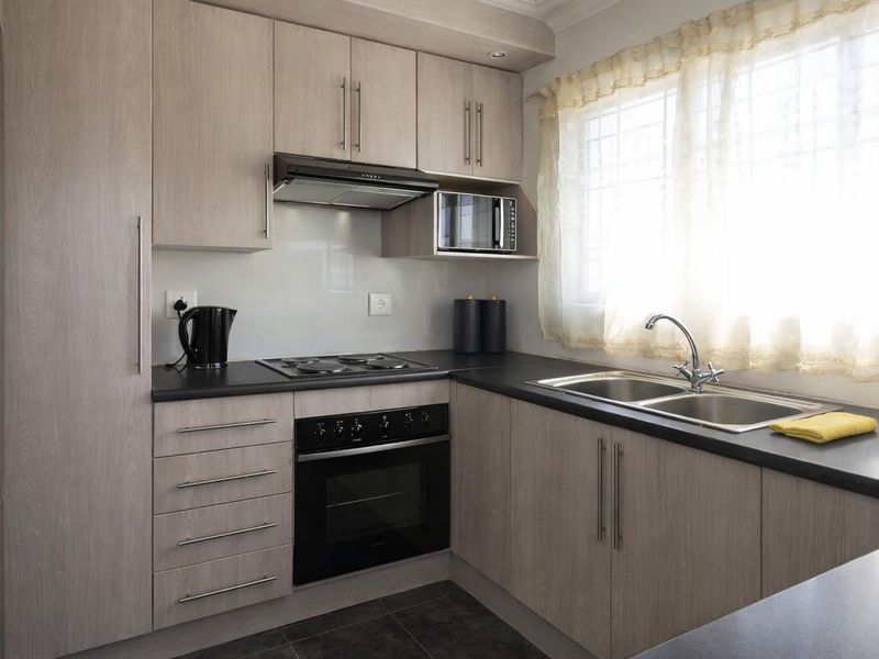 A well-maintained kitchen featuring light wood-look cabinetry, dark countertops, a built-in oven, hob, extractor fan, and a stainless steel double sink.