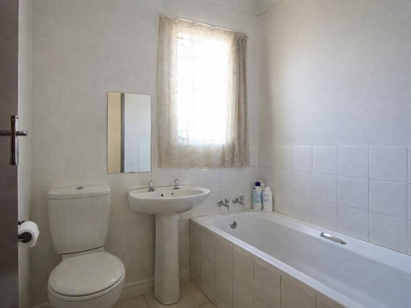 A functional bathroom featuring a pedestal basin, a built-in bathtub with tiled surround, and a standard toilet.