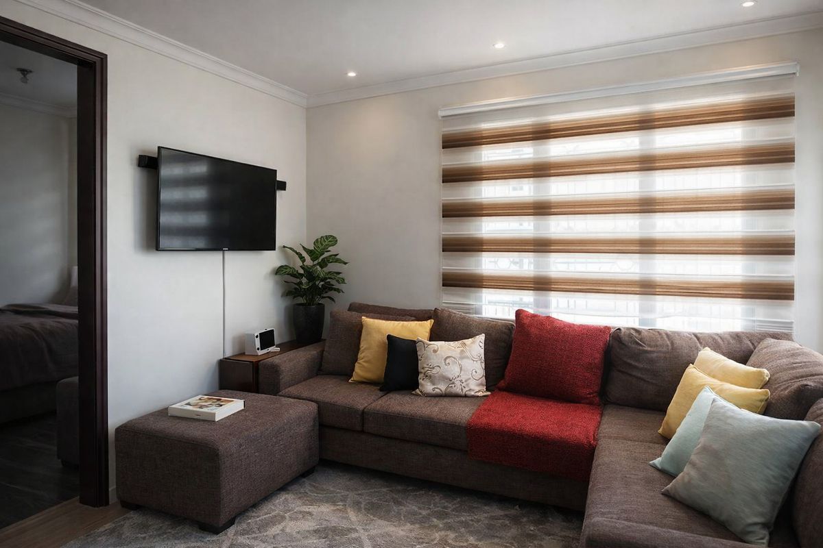 A well-maintained living room featuring recessed downlighting, modern roller blinds, and a wall-mounted television setup.