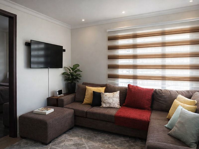 A well-maintained living room featuring recessed downlighting, modern roller blinds, and a wall-mounted television setup.