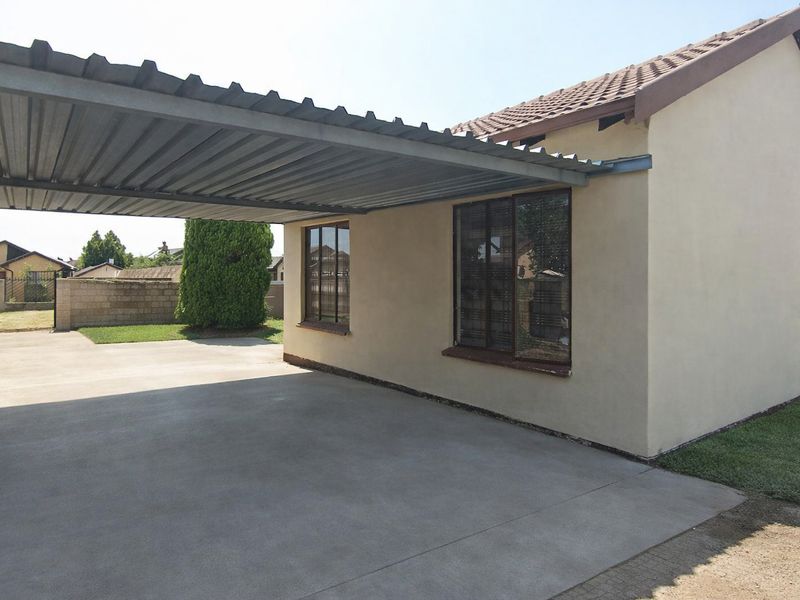 A functional carport area with a corrugated metal roof, concrete driveway, and secure boundary wall, providing convenient covered parking space.