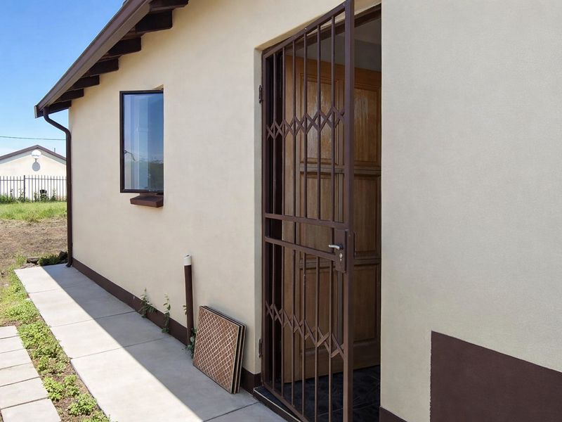 Rear exterior view of the property featuring a secure metal gate, timber entrance door, and a concrete walkway along the building perimeter.