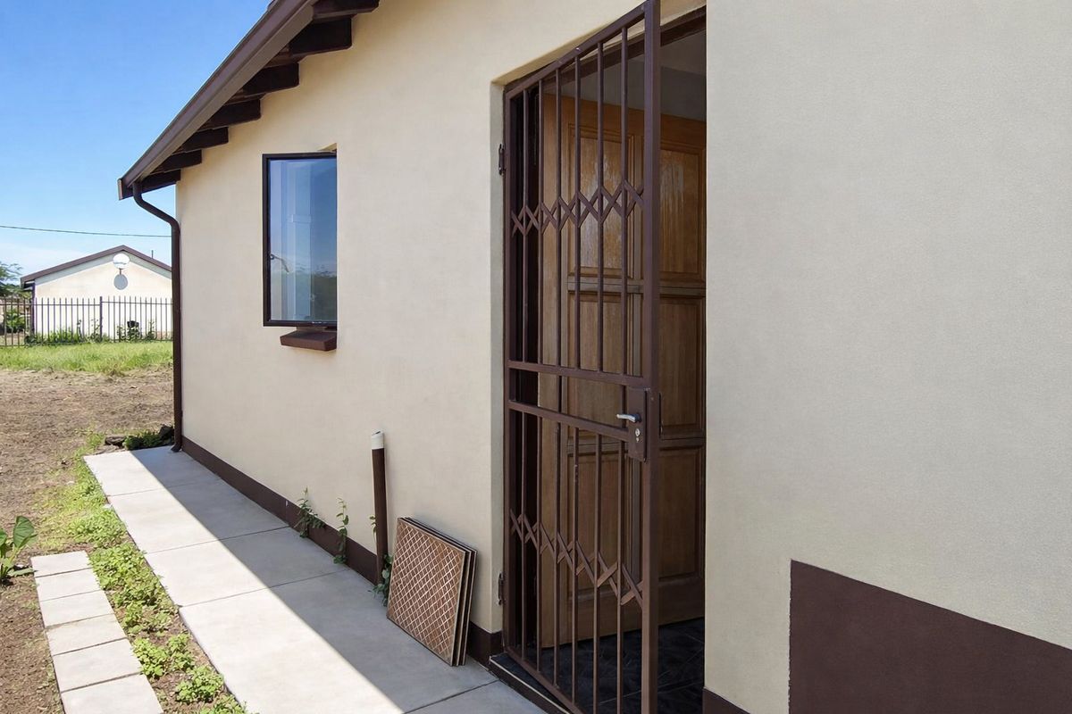 Rear exterior view of the property featuring a secure metal gate, timber entrance door, and a concrete walkway along the building perimeter.