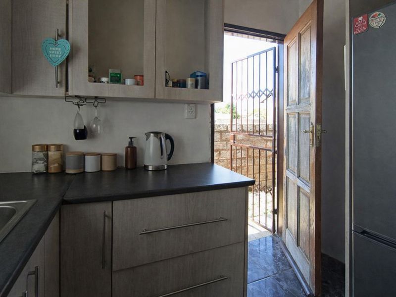 A functional kitchen area featuring laminate cabinetry, dark countertops, and direct access to an exterior space through a wooden door with a security gate.