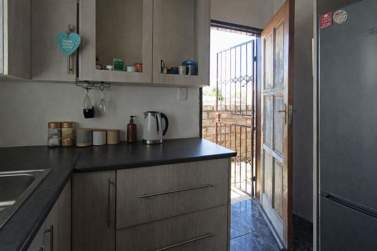 A functional kitchen area featuring laminate cabinetry, dark countertops, and direct access to an exterior space through a wooden door with a security gate.