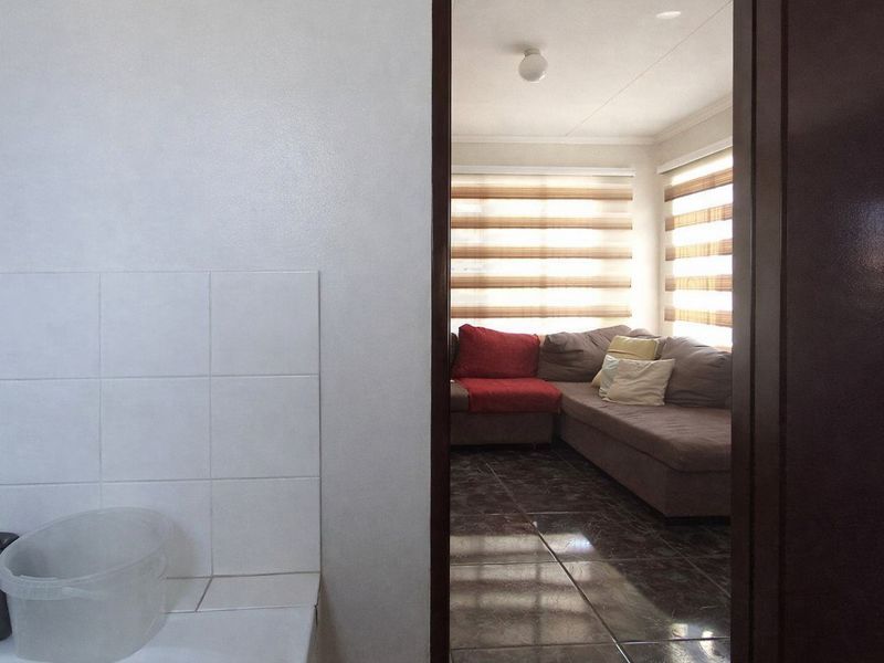 A view from an adjacent room looking into a living area featuring tiled flooring and modern roller blinds.