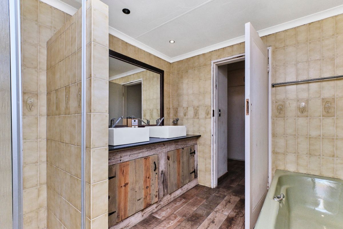 A bathroom featuring a double vanity with vessel sinks, a large mirror, and a bathtub, finished with neutral wall tiling.