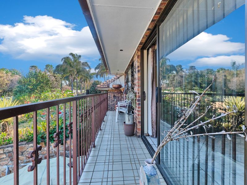 A covered balcony featuring tiled flooring, a metal balustrade, and sliding glass door access, overlooking a landscaped garden area.