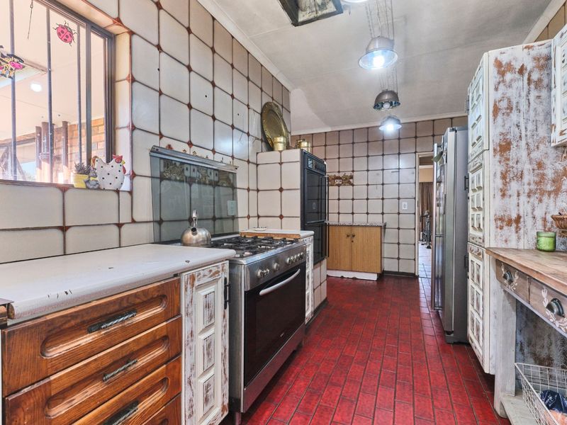 A dated kitchen featuring tiled walls, red tiled flooring, built-in cabinetry, and a gas stove with an integrated oven.