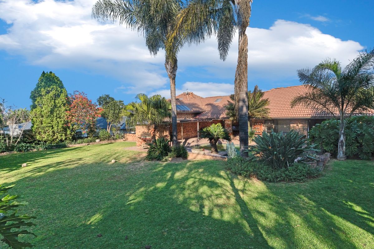 A spacious rear garden featuring a well-maintained lawn, mature palm trees, and a brick-built residence with a tiled roof and covered patio area.