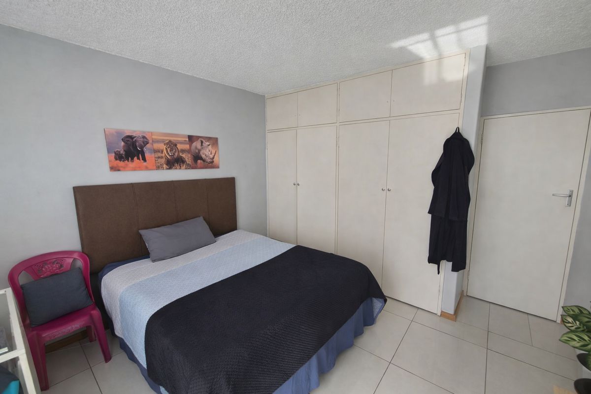 A bedroom featuring built-in cupboards, tiled flooring, and a textured ceiling, offering a functional space with potential for cosmetic updates.