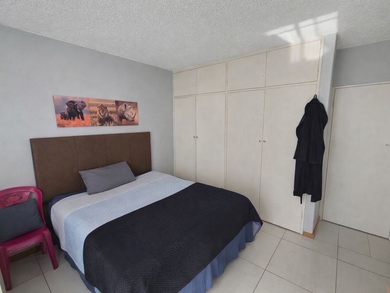A bedroom featuring built-in cupboards, tiled flooring, and a textured ceiling, offering a functional space with potential for cosmetic updates.