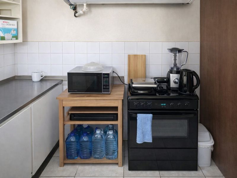 A functional kitchen area featuring a stainless steel countertop, tiled backsplash, and a black freestanding oven with hob.