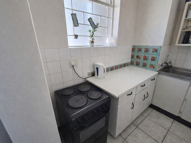 A compact kitchen featuring white cabinetry, a tiled backsplash, a stainless steel sink, and a freestanding electric stove.