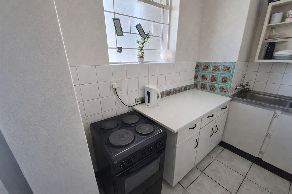 A compact kitchen featuring white cabinetry, a tiled backsplash, a stainless steel sink, and a freestanding electric stove.