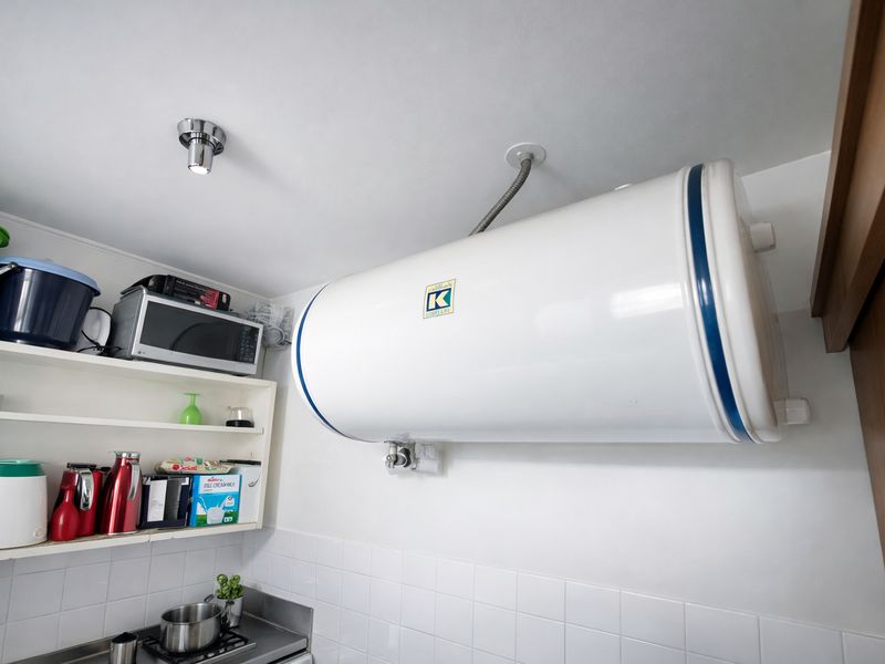 A utility area featuring a wall-mounted electric water heater, built-in shelving, and tiled splashback finishes.