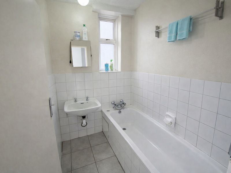 A functional bathroom featuring a white bathtub, wall-mounted basin, and neutral tiled finishes, providing a clean and practical space.