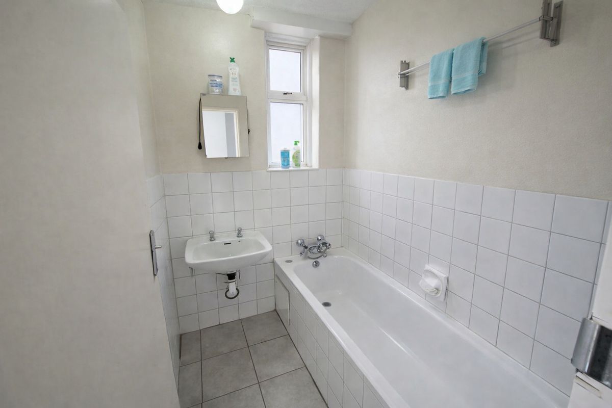 A functional bathroom featuring a white bathtub, wall-mounted basin, and neutral tiled finishes, providing a clean and practical space.