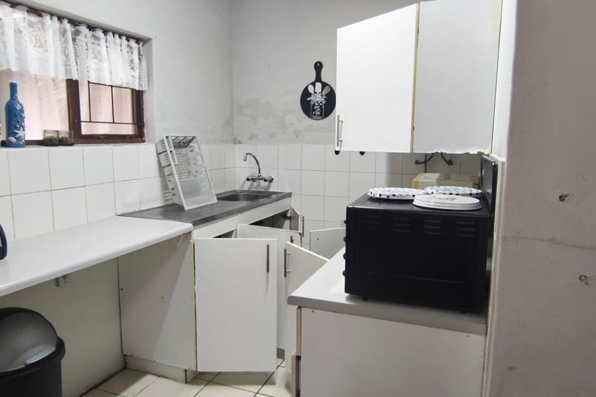 A dated kitchen featuring white cabinetry, tiled backsplash, and a stainless steel sink, requiring cosmetic updates and repairs to cabinetry.