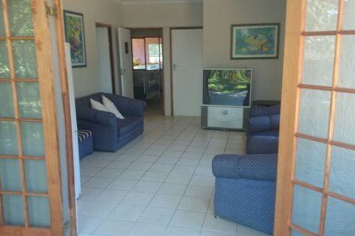 A living room featuring tiled flooring and wooden-framed french doors leading to an outdoor area.
