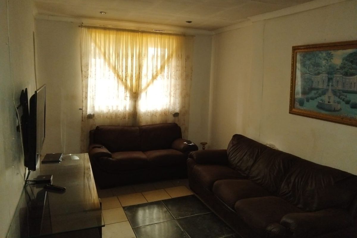 A living room featuring tiled flooring and recessed ceiling lighting, currently showing signs of wear on the wall surfaces.
