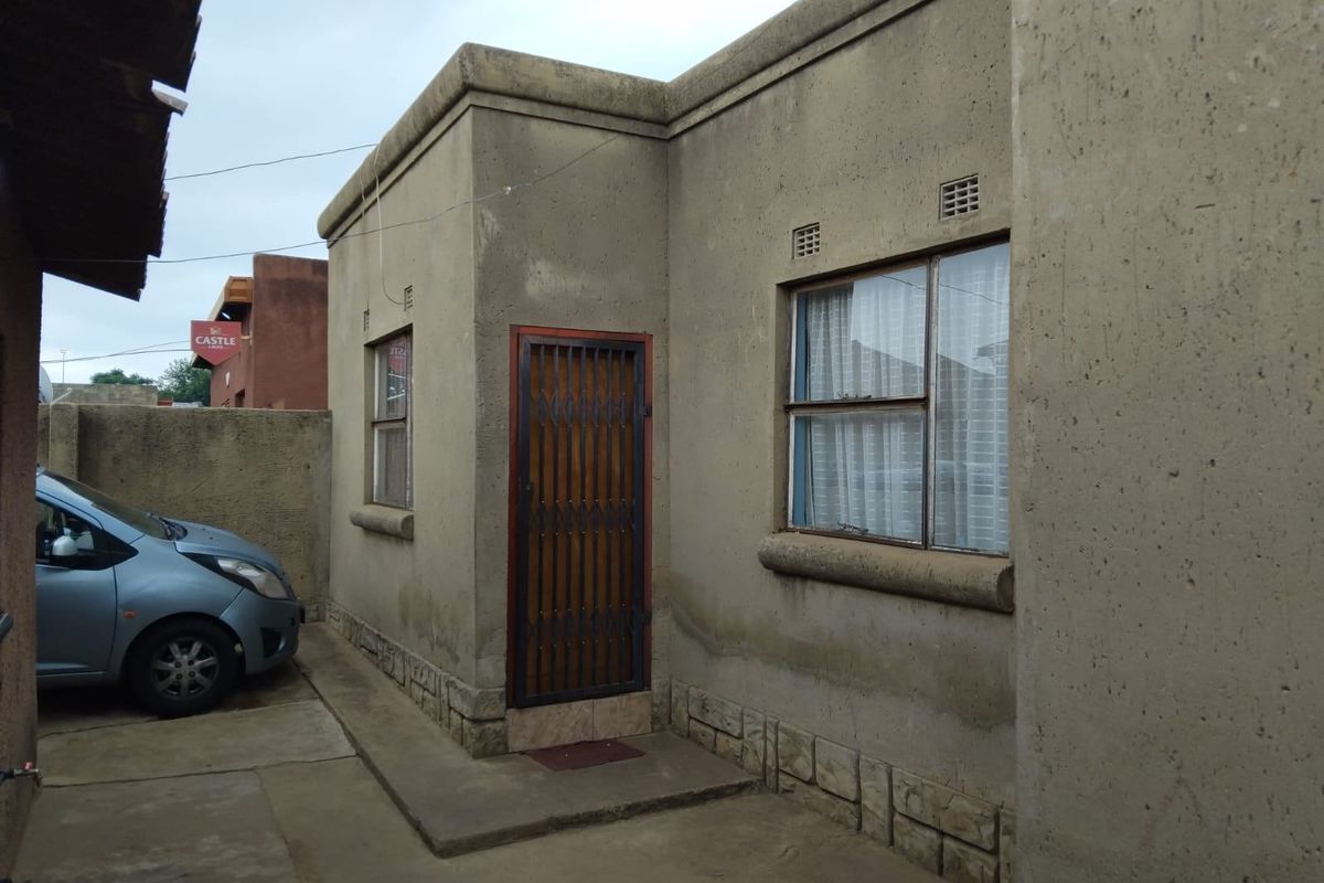 Rear exterior view of the property featuring cement rendered walls, metal window frames, and a security gate entrance.