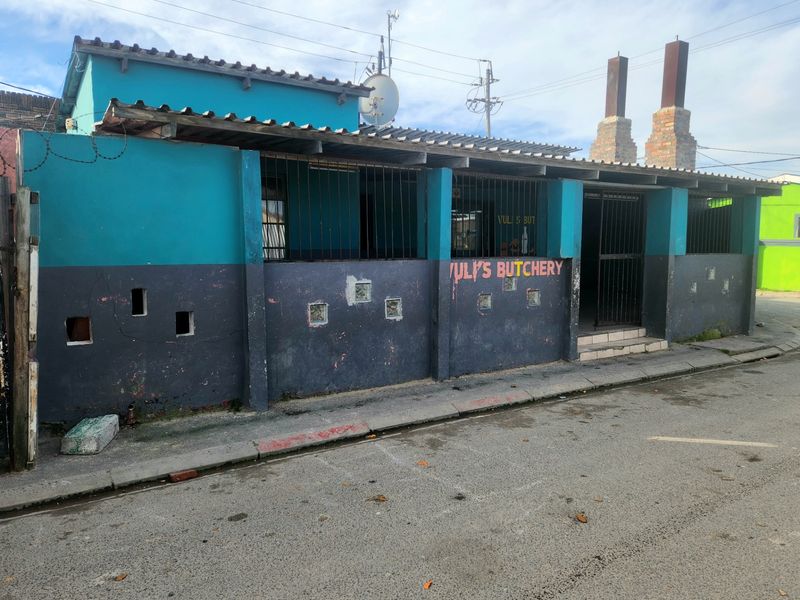 Front exterior view of a commercial-style building featuring a corrugated roof, security bars, and brick chimneys, showing signs of significant wear.