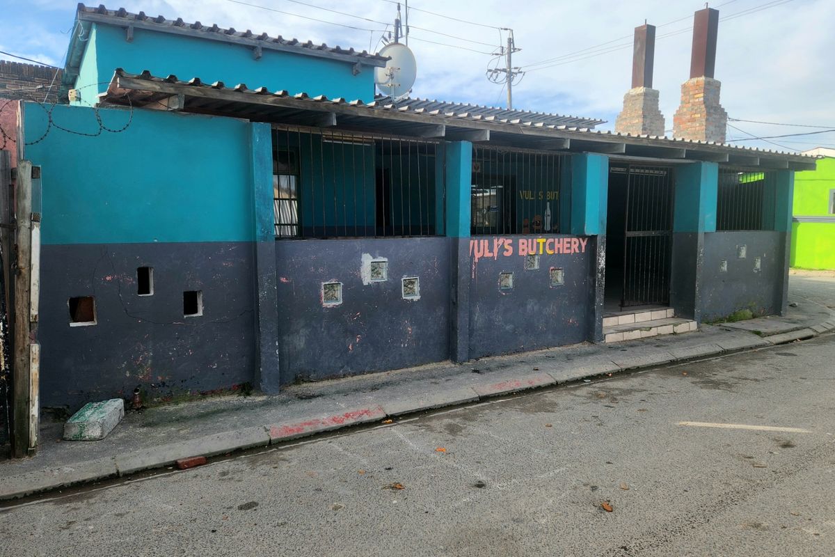 Front exterior view of a commercial-style building featuring a corrugated roof, security bars, and brick chimneys, showing signs of significant wear.