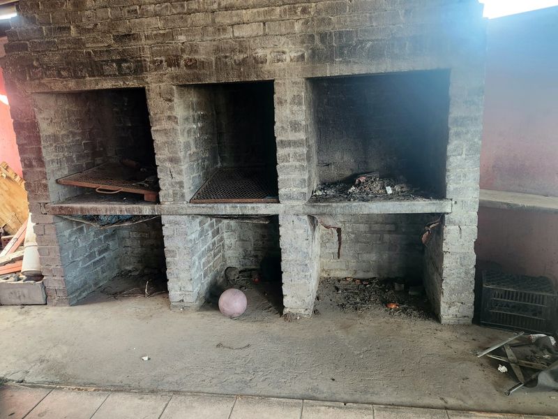 Outdoor patio area featuring a large, multi-bay built-in brick braai with concrete flooring, requiring maintenance and cleaning.