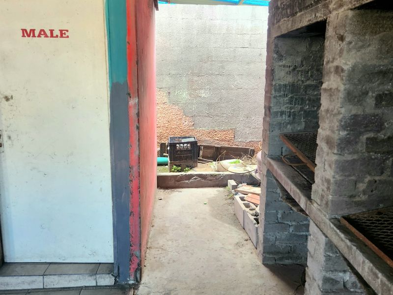 Outdoor patio area featuring a built-in brick braai, tiled and concrete flooring, and access to a utility area.