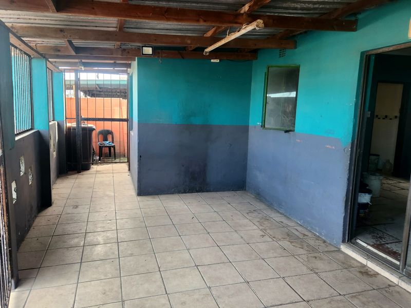 A covered outdoor patio area featuring tiled flooring, exposed timber roof beams, and security gates, requiring maintenance and cosmetic updates.