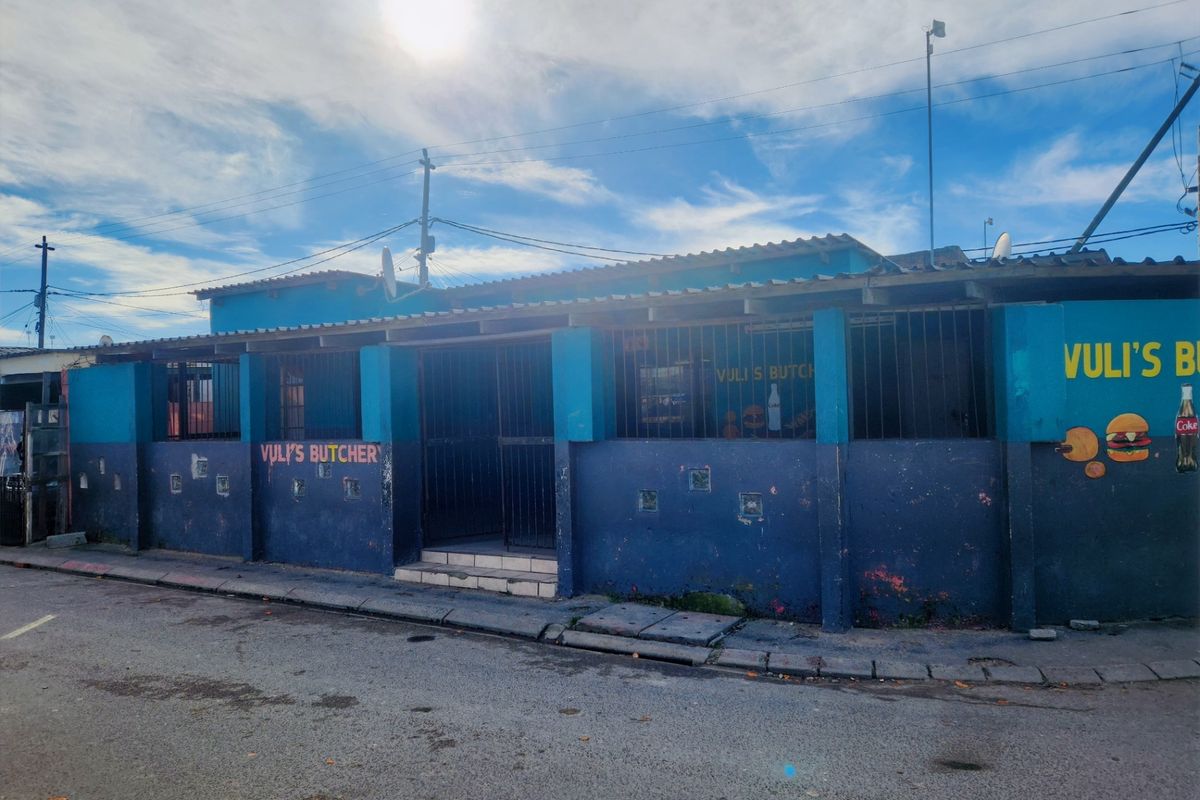 Street-facing view of a commercial property featuring a blue painted facade, security bars, and a tiled roof structure.