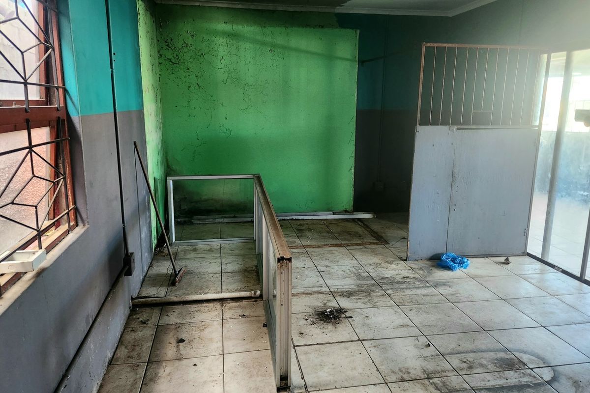 An empty, dilapidated interior space featuring tiled flooring, security window bars, and partition walls, requiring significant renovation and cosmetic repairs.